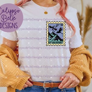 May include: White t-shirt with a graphic of a vintage postage stamp featuring a fantasy romance theme with a dragon and the text "Fantasy Romance".