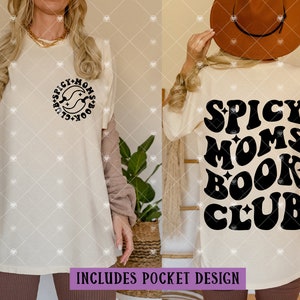 May include: A white t-shirt with a black graphic that says "Spicy Moms Book Club" in a retro font. The graphic is on the back of the shirt. The shirt is being modeled by a person wearing brown pants.