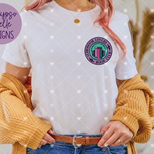 May include: White t-shirt with a purple and teal circle graphic that says "Audiobook Lovers Book Club" with a stack of books and headphones inside the circle.