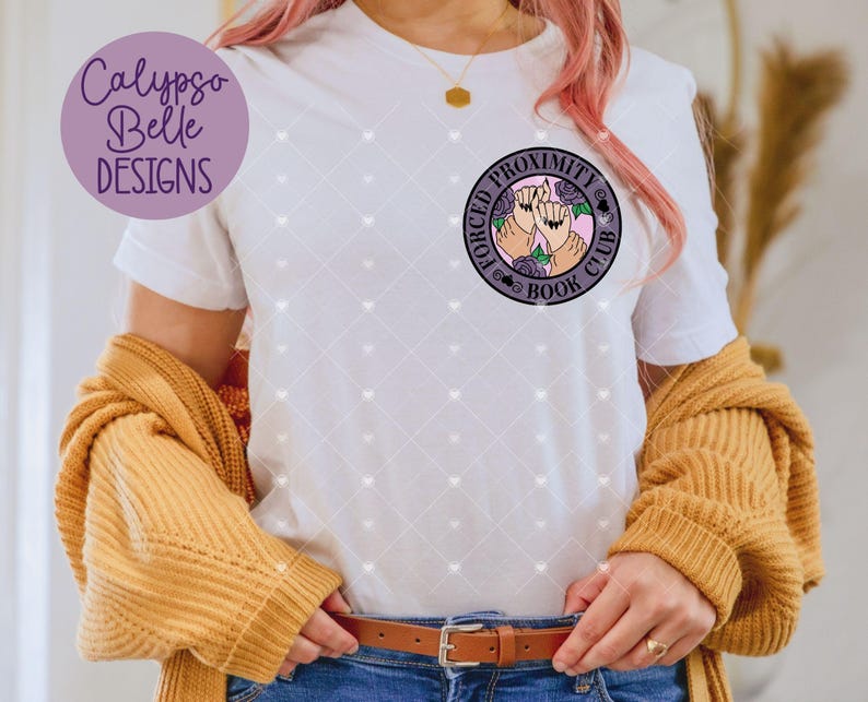 May include: White t-shirt with a round graphic that says "FORCED PROXIMITY BOOK CLUB" with two hands and roses. The shirt has a diamond pattern and the brand "Calypso Belle Designs" is on the left side. A mustard-colored sweater is draped over the shoulders.