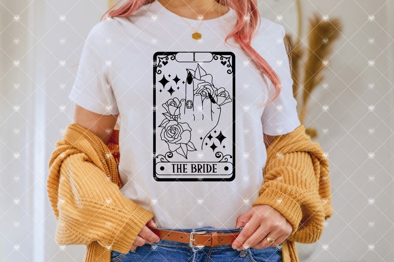 May include: A white t-shirt with a black and white illustration of a tarot card. The card is labeled "The Bride" and features a hand with a ring on the middle finger, surrounded by roses.
