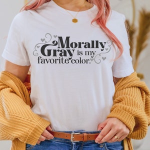 Pu&ograve; includere: Maglietta bianca con il testo "Morally Gray is my favorite color." in lettere nere con cuori e volute grigi.