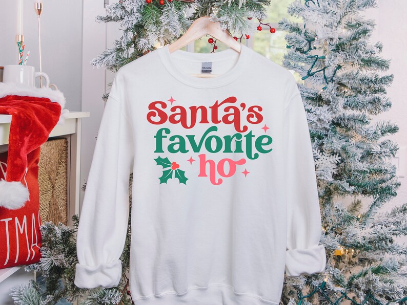 May include: White sweatshirt with a green holly leaf and red berry design. The text "Santa's favorite ho" is printed in red, green, and pink.