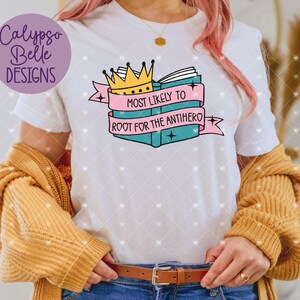 May include: White t-shirt with a pink and blue graphic of a book with a crown on top. The text on the graphic says "Most Likely to Root for the Antihero".