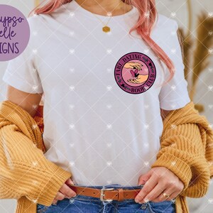 K&ouml;nnte beinhalten: Wei&szlig;es T-Shirt mit einem rosafarbenen Kreis-Motiv, auf dem "Fave Dating Book Club" steht. Das Motiv zeigt zwei H&auml;nde, die ein Herz mit einem Schmetterling halten.