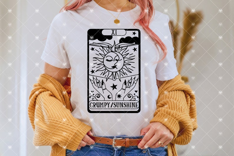 May include: A white t-shirt with a black and white illustration of a tarot card. The card is the "XI" card, and it features a sun and moon with a face, and the text "GRUMPY/SUNSHINE".