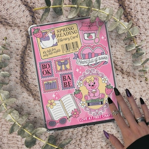 May include: A pink tablet case with a whimsical design featuring strawberries, a teddy bear, and the text "Spring Reading Library Card." Other text includes "Heart full of books" and "Love at first chapter."