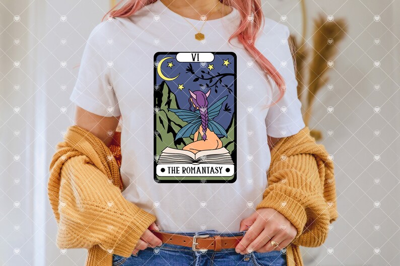May include: White t-shirt with a graphic of a tarot card featuring a fairy reading a book. The card is labeled "VI THE ROMANTASY".