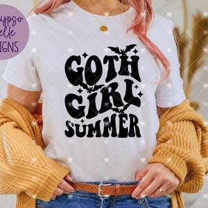 May include: White t-shirt with a black graphic that says "goth girl summer" with bats and stars around the text.