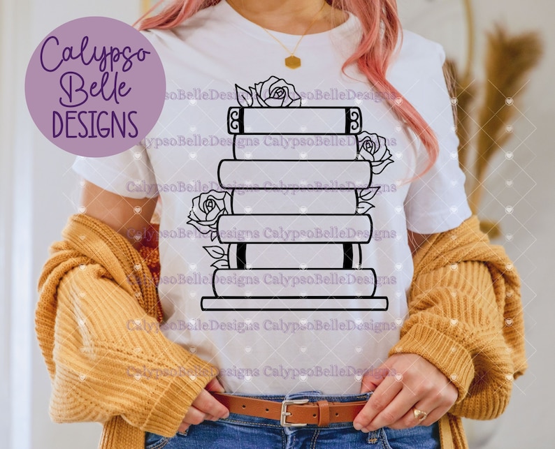 May include: A white t-shirt with a black outline of a stack of books with roses on the side. The text "Calypso Belle Designs" is on the shirt.