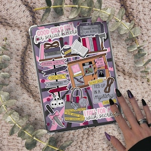 Op de afbeelding: Een doorzichtige tablethoes versierd met stickers met een mysterie thema. De stickers bevatten tekst als "Good Girls Fall for Serial Killers" en "Tied Up in a Mystery." De hoes heeft een paarse en roze gestreepte achtergrond.