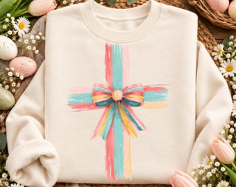 Peut inclure: Un sweat-shirt à col rond couleur crème arborant un motif central en forme de croix, composé de coups de pinceau verticaux et horizontaux dans des tons rose, bleu sarcelle et jaune, avec un nœud rayé multicolore au centre.