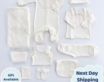 May include: A set of 10 off-white baby clothes, including a onesie, a shirt, a sleeveless shirt, pants, a hat, a blanket, a bib, mittens, and a pair of socks.