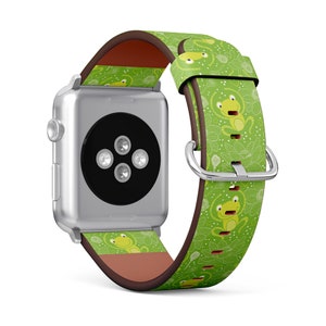 May include: A silver Apple Watch with a green leather strap. The strap has a repeating pattern of cartoon frogs and white floral designs. The strap has a brown underside and a silver buckle.