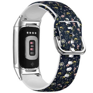 Peut inclure: Un tracker de fitness argenté et blanc avec un bracelet à motif floral bleu foncé et blanc. Le tracker a un écran noir avec un motif de points blancs et trois petites lumières roses.