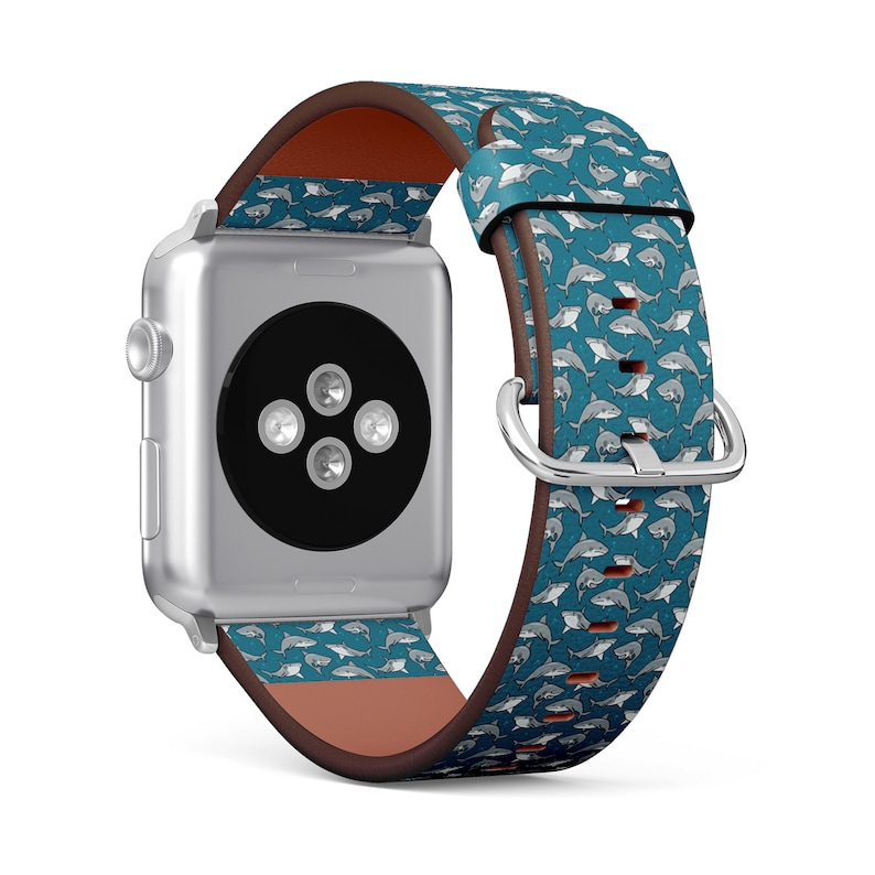 May include: A silver Apple Watch with a blue and white shark print band. The band is made of leather and has a brown leather lining.