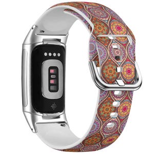 May include: A Fitbit fitness tracker with a white and patterned band. The band features a colorful, intricate design with orange, purple, and yellow hues. The tracker has a black screen and a silver frame.