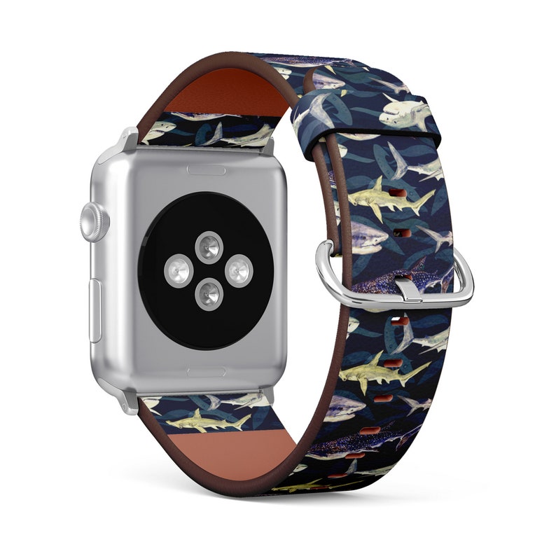 Pode incluir: Um Apple Watch prateado com uma pulseira de couro com estampa de tubar&otilde;es azul e branco. A pulseira tem um forro de couro marrom.
