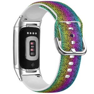 Op de afbeelding: Een Fitbit-fitnesstracker met een witte en regenboogkleurige band. De band heeft een gespikkeld patroon met een spectrum aan kleuren, waaronder geel, groen, blauw en paars. De tracker heeft een zwart scherm en een zilverkleurig frame.