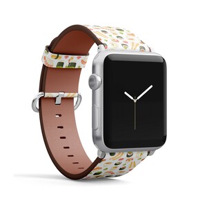 Pode incluir: Um Apple Watch branco com uma pulseira de couro marrom com um padr&atilde;o de sushi colorido. O mostrador do rel&oacute;gio &eacute; preto com ponteiros dourados.