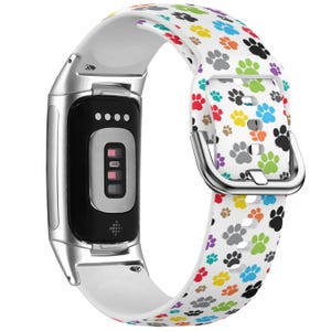 May include: White silicone watch band with a colorful paw print pattern. The band is compatible with Samsung Galaxy Fit 2 smartwatches.