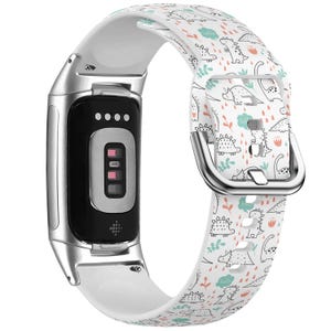 May include: A white silicone watch strap with a dinosaur print. The strap has a silver buckle and is compatible with Fitbit Inspire 2 and Inspire HR fitness trackers.