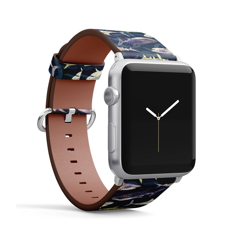 Pode incluir: Um Apple Watch prateado com uma pulseira de couro azul escuro e branco com estampa de tubar&atilde;o. O mostrador do rel&oacute;gio &eacute; preto com ponteiros brancos.