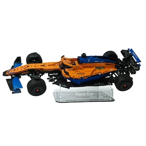 May include: An orange and blue race car model with black wheels and a clear display stand. The model is a detailed replica of a McLaren Formula 1 car. The stand has the text "McLaren Formula 1 Race Car".