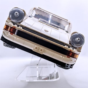May include: A white Lego Porsche 911 Turbo model with black accents and clear headlights. The car is displayed on a clear acrylic stand.
