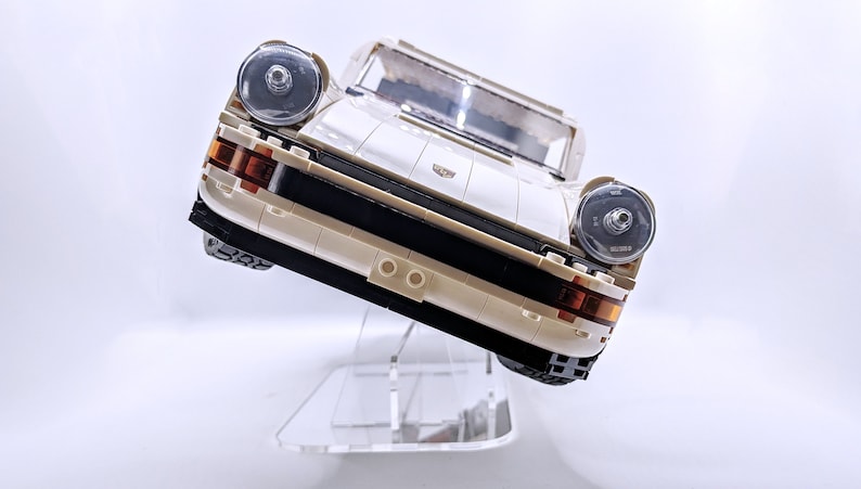 May include: A white Lego Porsche 911 Turbo model with black accents and clear headlights. The car is displayed on a clear acrylic stand.