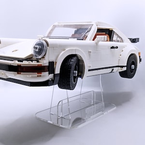 May include: A white Lego Porsche 911 Turbo model car on a clear acrylic display stand. The car has black wheels and a black stripe along the side.
