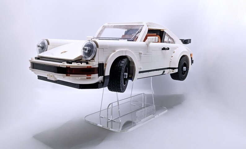 May include: A white Lego Porsche 911 Turbo model car on a clear acrylic display stand. The car has black wheels and a black stripe along the side.