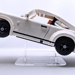May include: A white Lego Porsche 911 Turbo model car on a clear acrylic display stand. The car is tilted at an angle, with the front wheels off the ground.