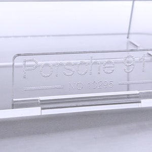 May include: A clear plastic display case with the text "Porsche 911 - NO 10295" etched into the front.