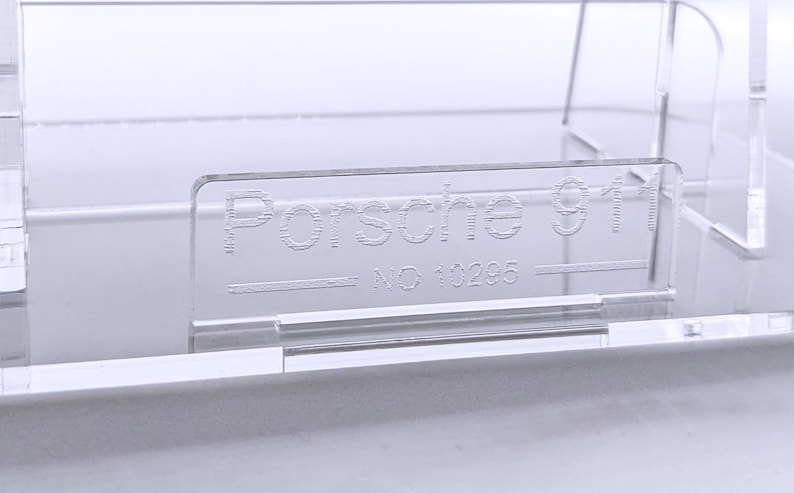 May include: A clear plastic display case with the text "Porsche 911 - NO 10295" etched into the front.