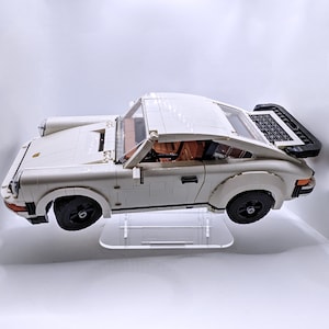 May include: A white Lego Porsche 911 Turbo model car on a clear display stand. The car has black wheels and a black rear spoiler.
