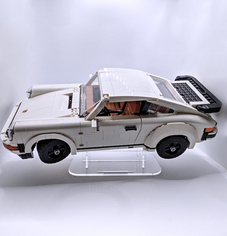 May include: A white Lego Porsche 911 Turbo model car on a clear display stand. The car has black wheels and a black rear spoiler.