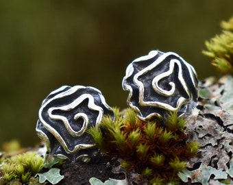 May include: A pair of silver earrings with a textured, abstract design. The earrings are in the shape of a swirl or a flower.