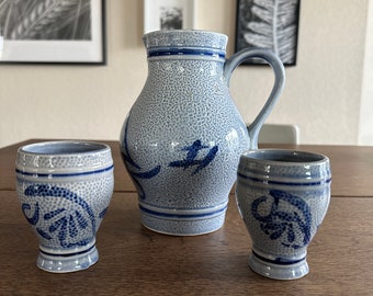 May include: Three blue and white ceramic mugs with a floral design. The mugs are on a wooden table.