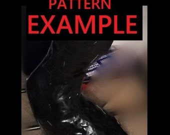 May include: A close-up of a black leather boot with a shiny finish. The boot is lying on a light brown surface.