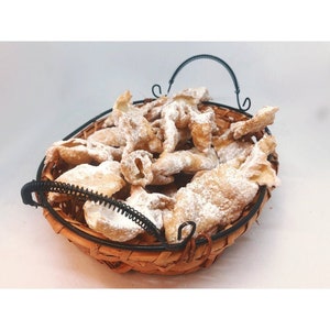 May include: A wicker basket filled with golden-brown, fried pastries dusted with powdered sugar. The basket has a black metal handle and rim. The pastries are a traditional dessert, perfect for a sweet treat.