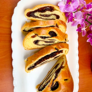 May include: A white platter with five slices of sweet bread with a swirl of dark chocolate filling. The bread is arranged in a row with the largest slice at the bottom. The platter is on a wooden surface.
