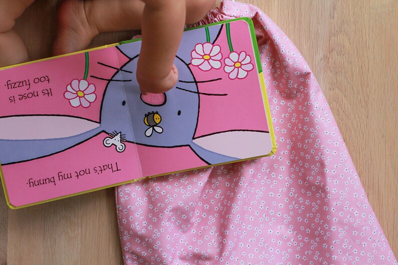 K&ouml;nnte beinhalten: Ein Kinderbuch mit einem rosa Einband und einem Bild eines blauen Hasen mit einer Biene auf der Nase. Der Text auf der Seite lautet "Das ist nicht mein Hase. Seine Nase ist zu flauschig."