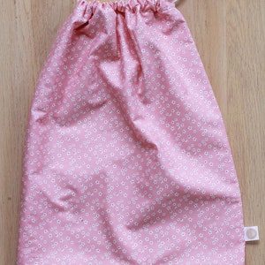 K&ouml;nnte beinhalten: Eine rosa Kordeltasche mit einem wei&szlig;en Blumenmuster. Die Tasche hat eine wei&szlig;e Kordel und ein kleines wei&szlig;es Etikett.