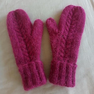 May include: A pair of magenta-colored knitted mittens. The mittens feature a cable knit design on the top and a ribbed cuff. The mittens are made of a soft, textured yarn, perfect for keeping hands warm in cold weather.