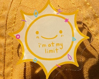 Op de afbeelding: Een gele baseballcap met een wit Adidas-logo en een gele zon-sticker met de tekst "I'm at my limit".