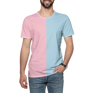 Peut inclure: T-shirt à manches courtes divisé en deux couleurs : rose clair et bleu clair. La personne porte un jean bleu et une montre. La chemise est portée par une personne avec une barbe.
