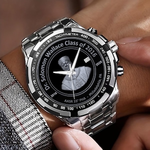 May include: A silver wristwatch with a black bezel and a stainless steel band. The watch face features a portrait and the text "Dr. Solomon Wallace Class of 2016". The watch has a tachymeter and various dials.