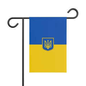 May include: A blue and yellow garden flag with the Ukrainian coat of arms, a trident, in the center. The flag is attached to a black metal pole.