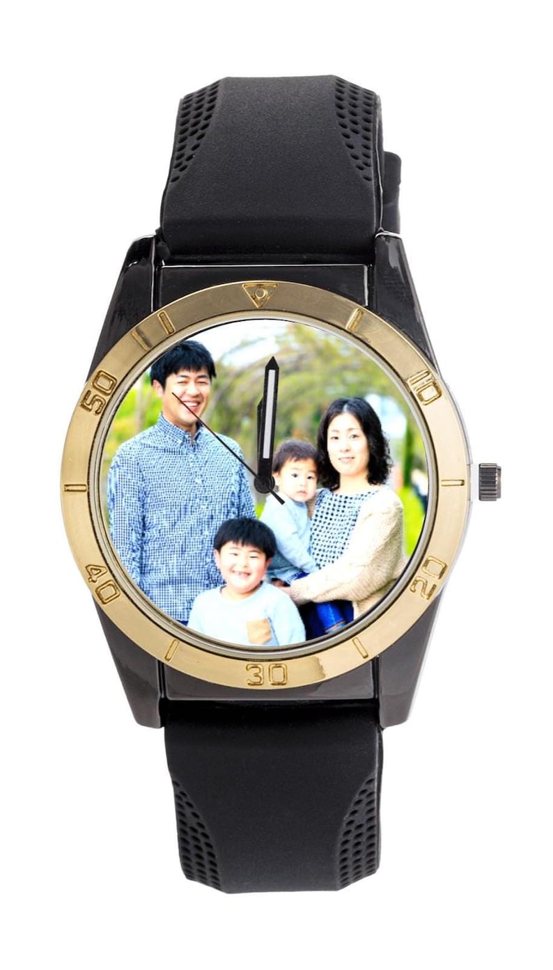 May include: Black wristwatch with a gold-coloured bezel and a black strap. The watch face displays a family portrait. The watch has a black dial with white numerals and hands.